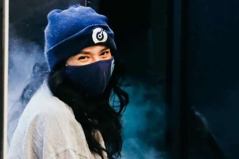 Woman with a beanie and a mask smiling.